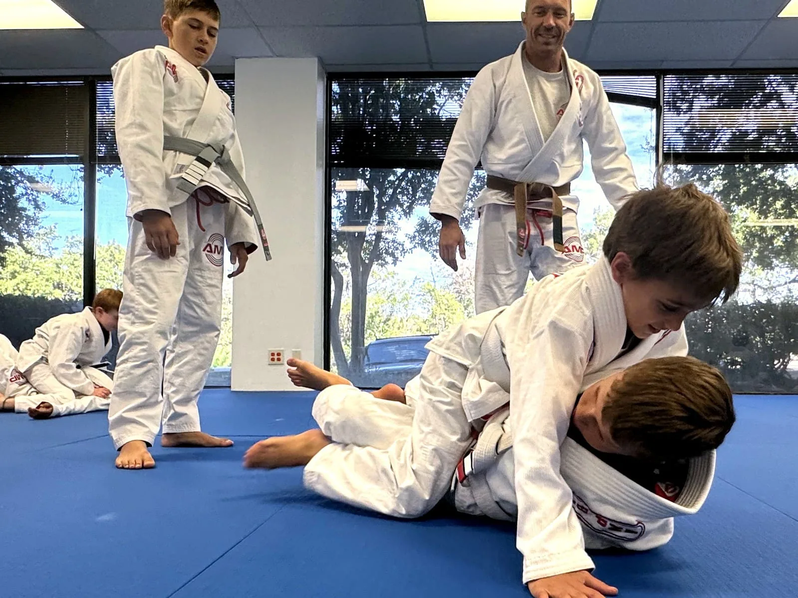 AMP BJJ coach watching two kids work a live grappling position while a teammate observes during a Constraints-Led Approach class