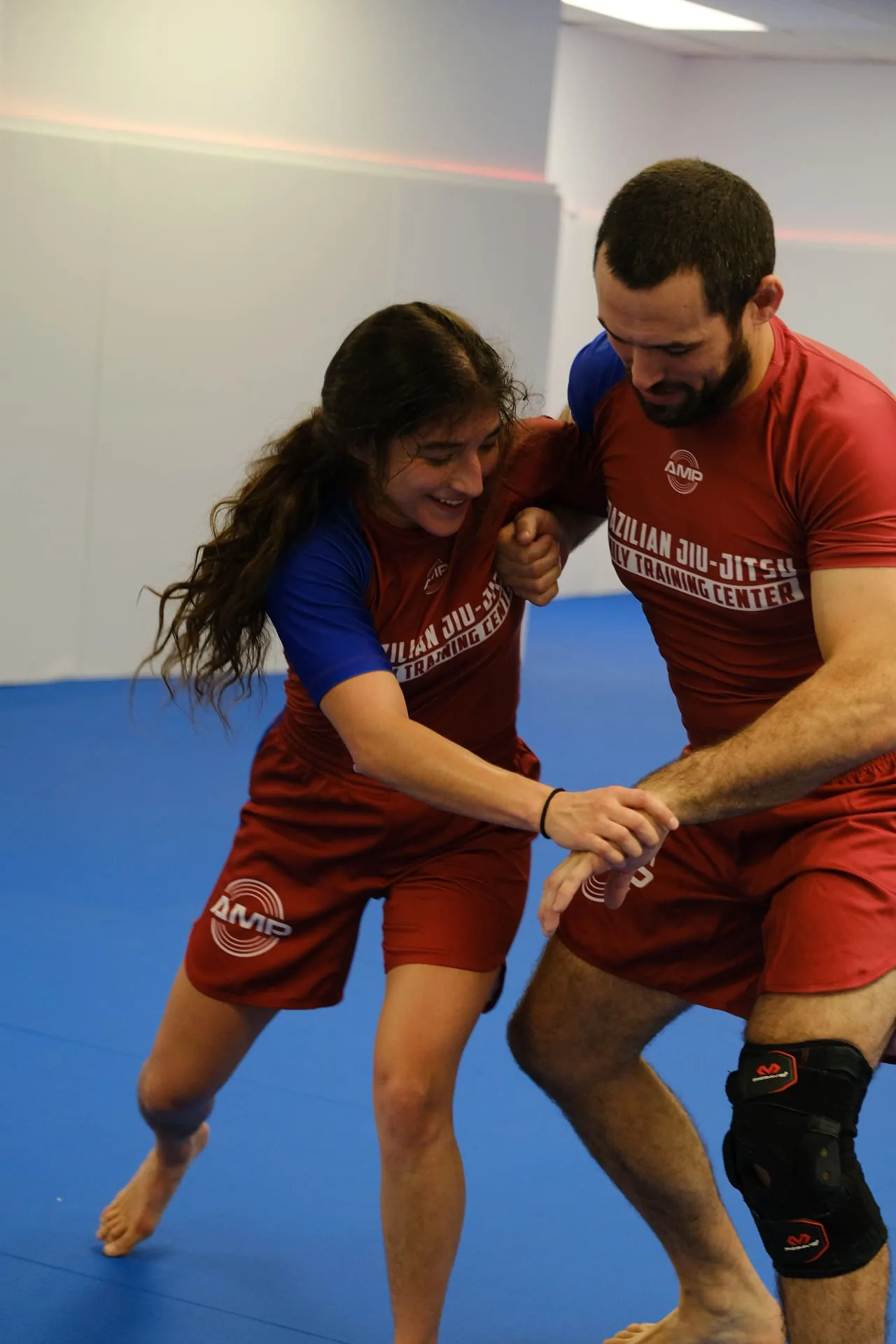 Two AMP BJJ students laughing while drilling a standing grip exchange on the blue mats