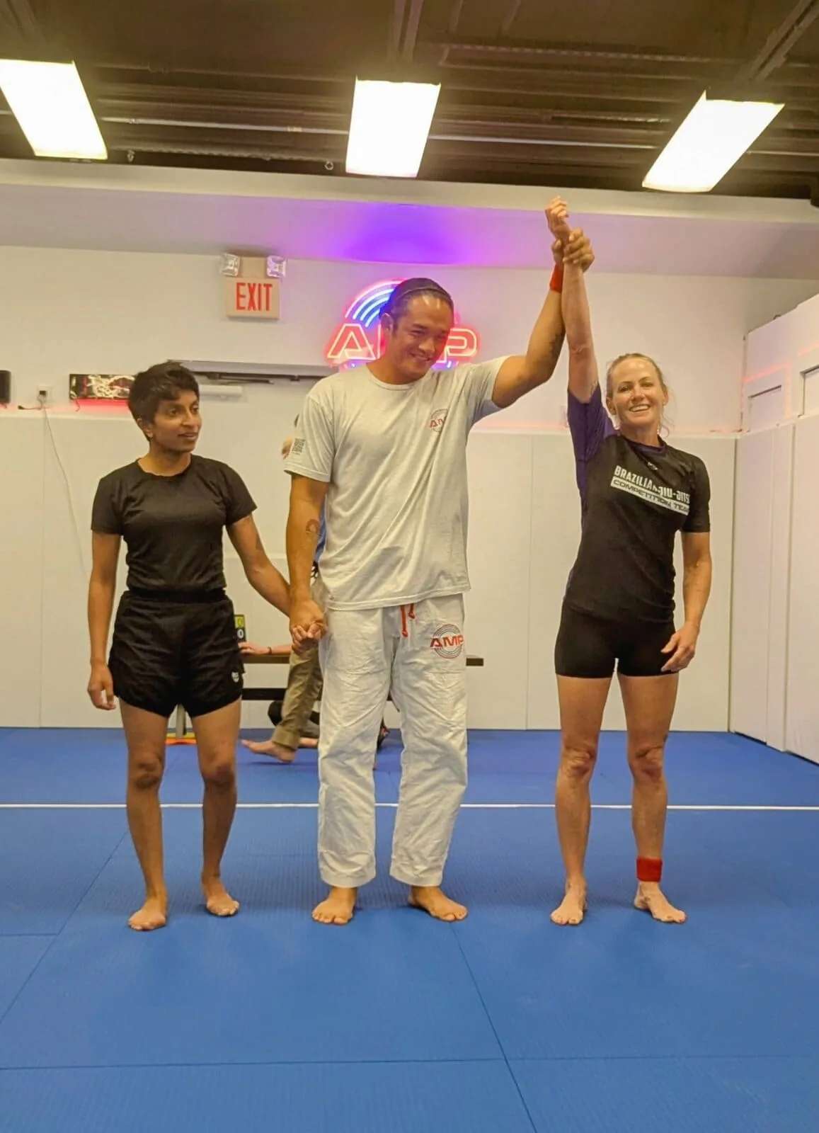AMP BJJ adult women competitors with the coach raising the winner's hand after a competition team match