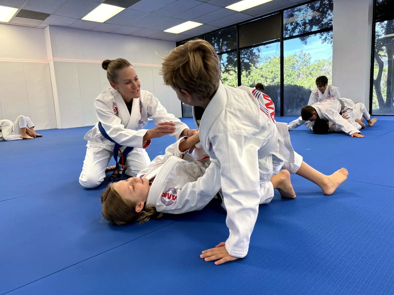 AMP BJJ mom coaching her child through a live grappling position on the blue mats next to other families training