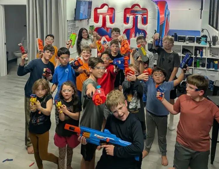 A group of excited kids at an AMP BJJ Parents' Night Out, wearing protective glasses and holding Nerf blasters, ready for an action-packed celebration.